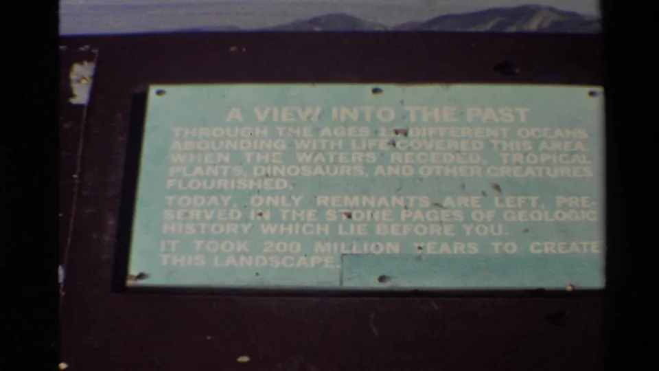 1980 8mm frame of a green geologic-history plaque titled A View Into The Past at an outdoor Western USA scenic stop.
