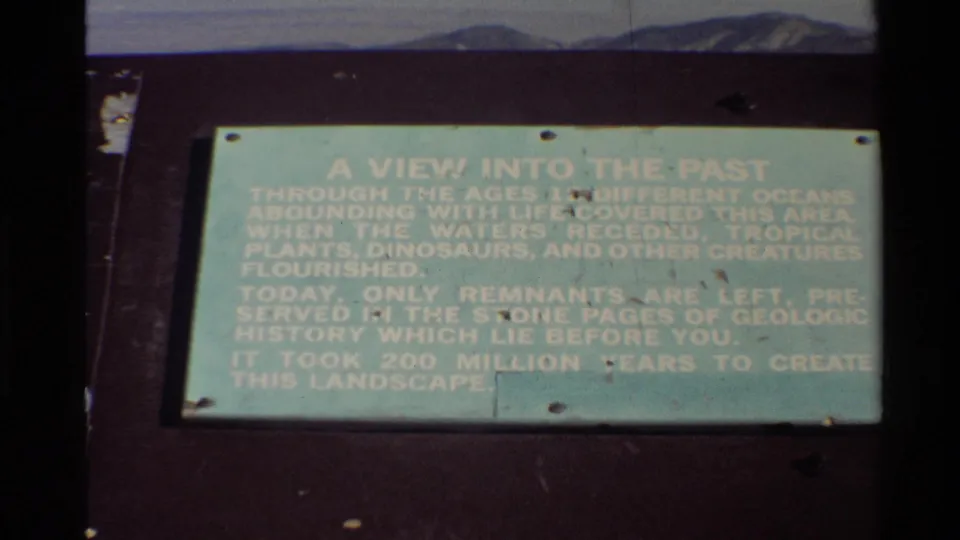 Visitor-shot 1980 8mm frame of a weathered geologic-history plaque with text about ancient oceans, plants, and dinosaurs.