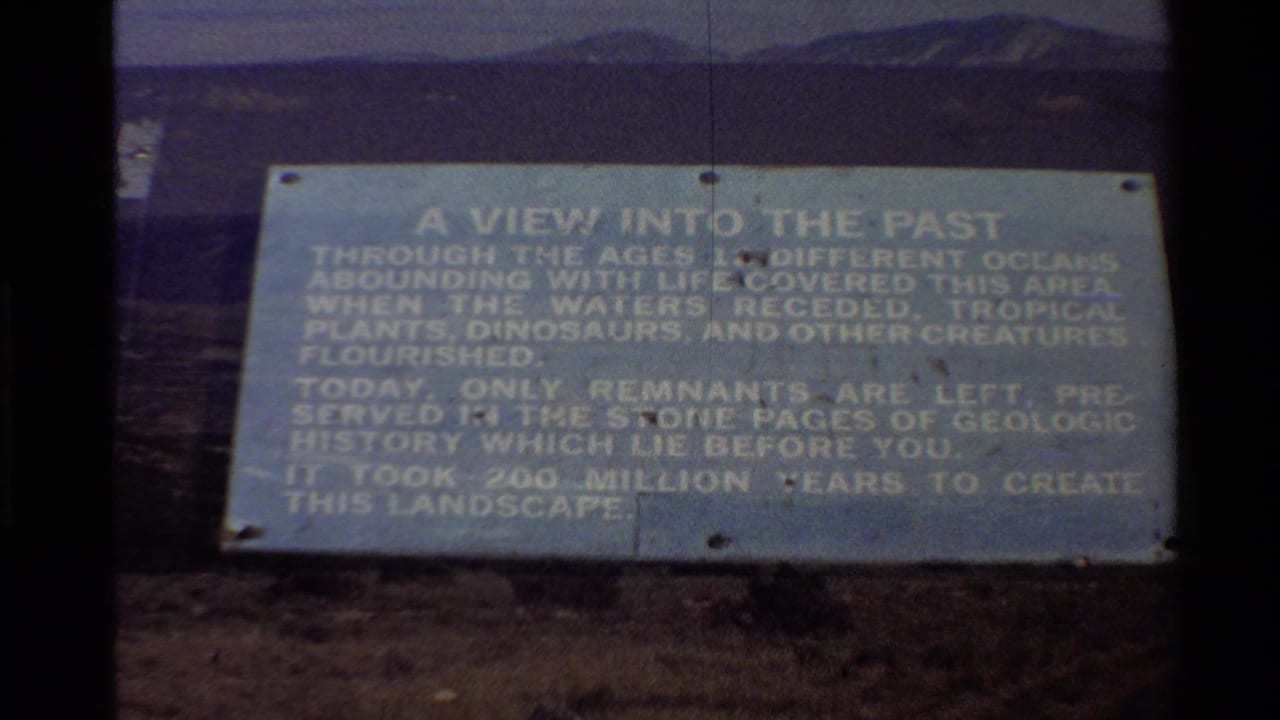 Interpretive sign in front of open terrain and distant mountains under a blue sky.