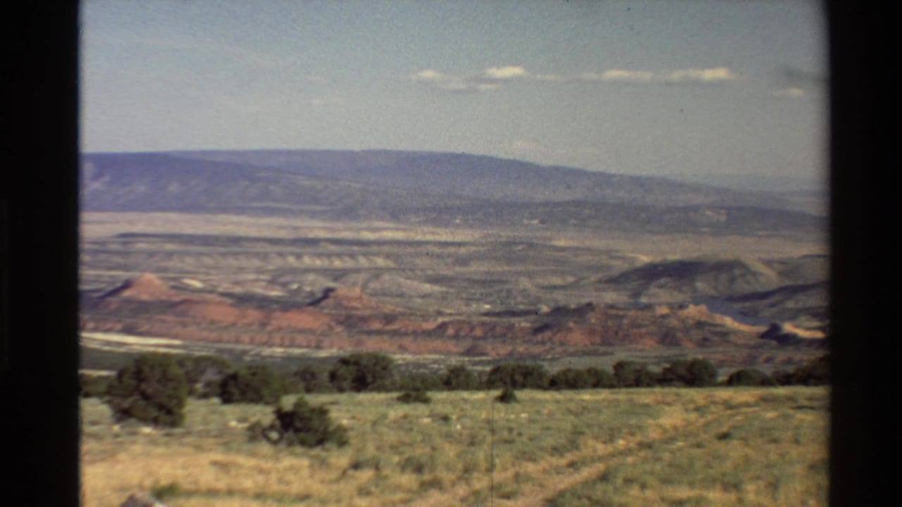 Final frame holds on the Western U.S. desert vista, showing low shrubs, layered red rock, a broad distant ridge, and clear sky in faded 8mm color.