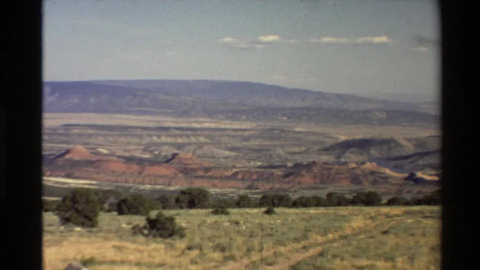 Final frame holds on the Western U.S. desert vista, showing low shrubs, layered red rock, a broad distant ridge, and clear sky in faded 8mm color.
