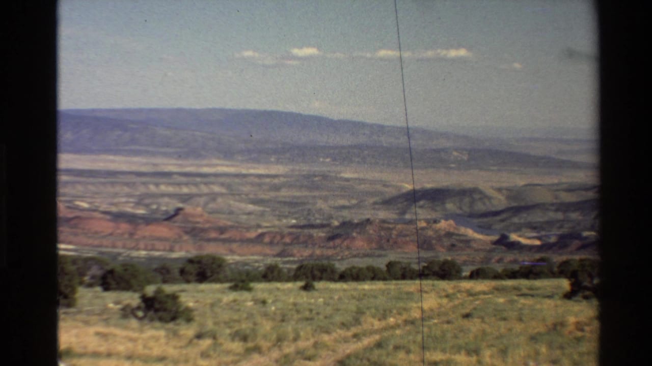 1980 8mm home-movie frame showing a Western U.S. desert valley from a high vantage point, with grassland, shrubs, hills, and sky.
