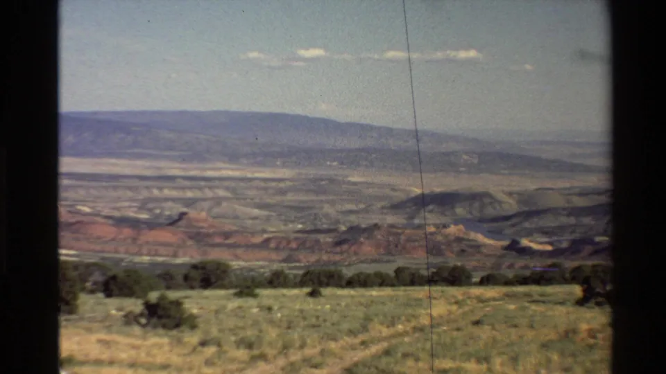 1980 8mm home-movie frame showing a Western U.S. desert valley from a high vantage point, with grassland, shrubs, hills, and sky.