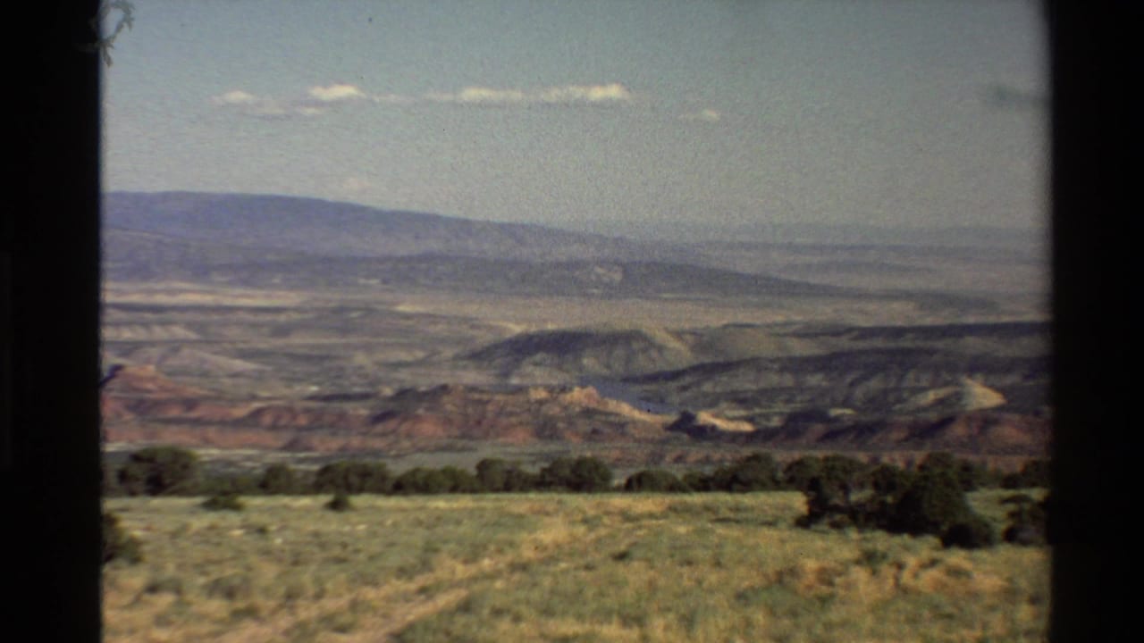 Panoramic view across scrubby grassland toward layered hills and distant mountains.