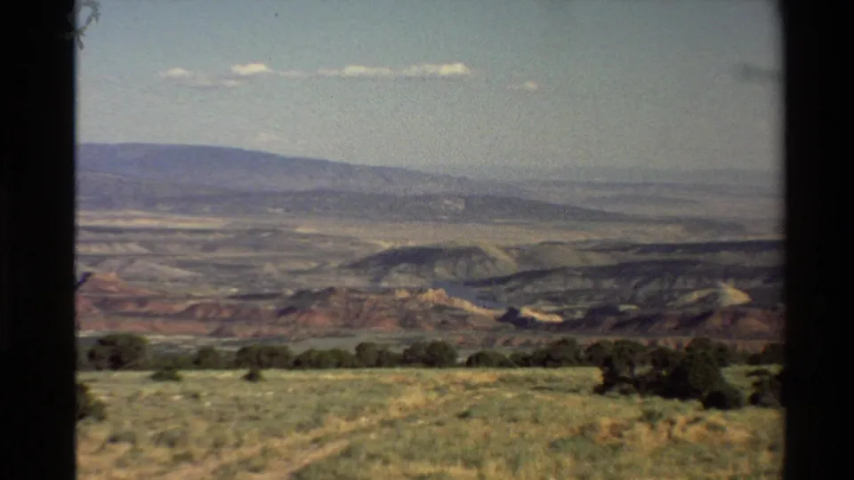 Western U.S. landscape view on 8mm film, looking over scrubby foreground grass toward layered hills and distant mountains.