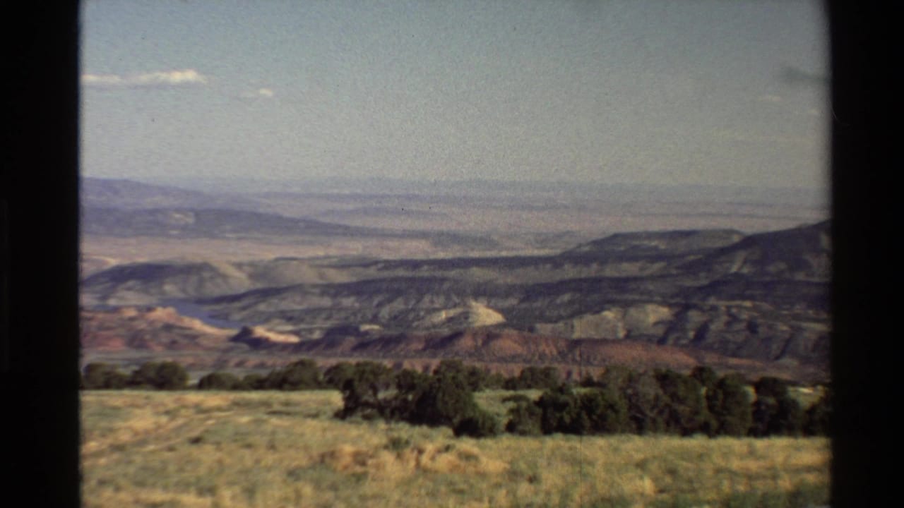 Western U.S. 8mm landscape frame with an arid foreground, dark ridgelines, a broad valley, and pale distant mountains.