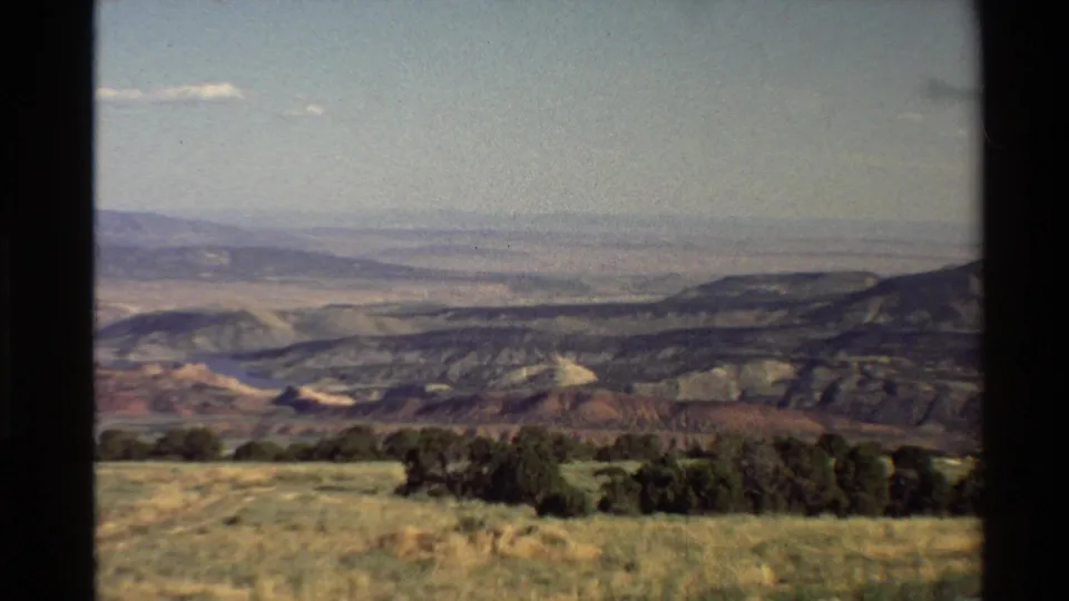 Western U.S. 8mm landscape frame with an arid foreground, dark ridgelines, a broad valley, and pale distant mountains.