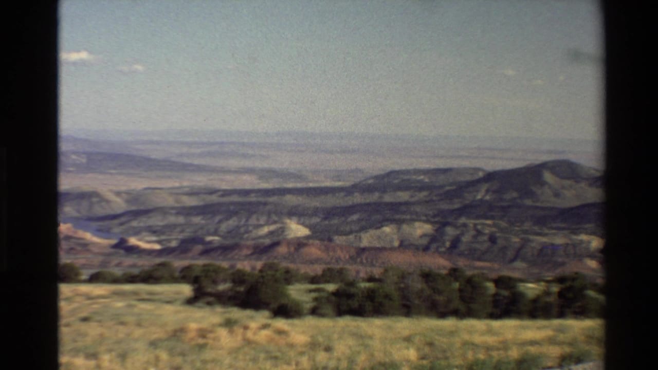 Western USA 1980 home-movie frame showing dry grass, shrubs, and layered mountain ridges seen through dark frame edges.