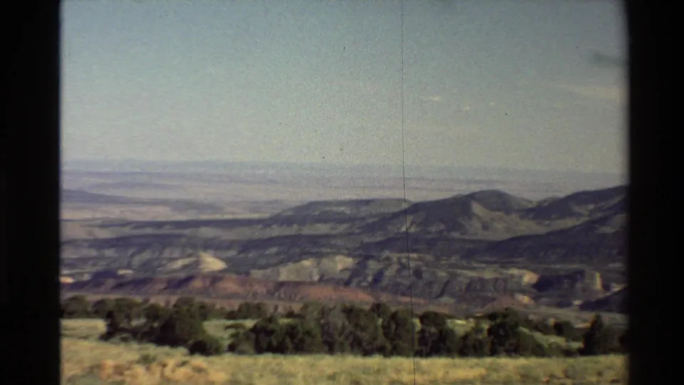 Western USA 1980 8mm view of a mountain ridge and broad valley beyond a grassy, shrub-lined foreground.