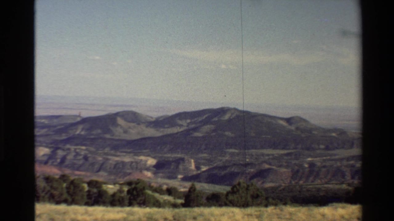 Western USA 1980 8mm frame showing a mountain range, dry foreground grass, shrubs, and dark vertical edges from the filming setup.