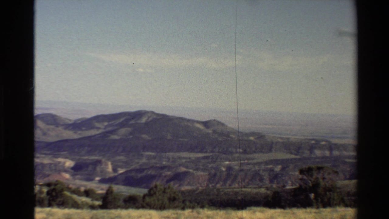 Mountain range and distant plain framed by dark vertical borders and low vegetation.