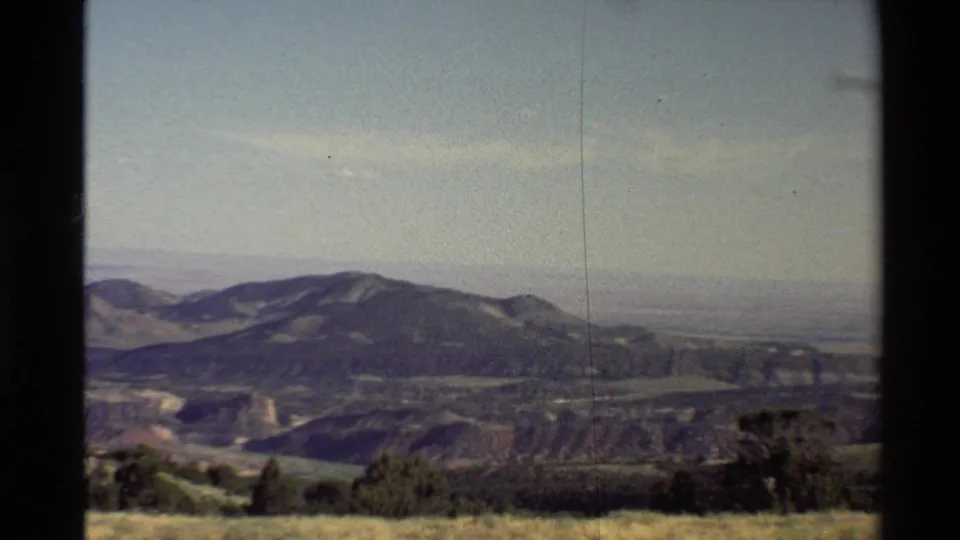 1980 8mm Western U.S. travel view of a mountain range, hazy plains, shrubs, and dark frame or window edges.