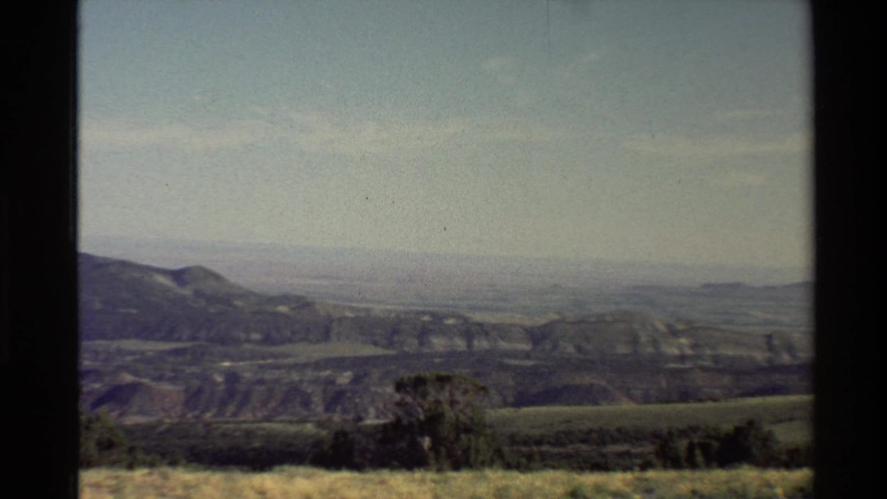 Western U.S. 1980 home-movie still showing low vegetation, rolling mountain ridge, distant plain, haze, and light blue sky.