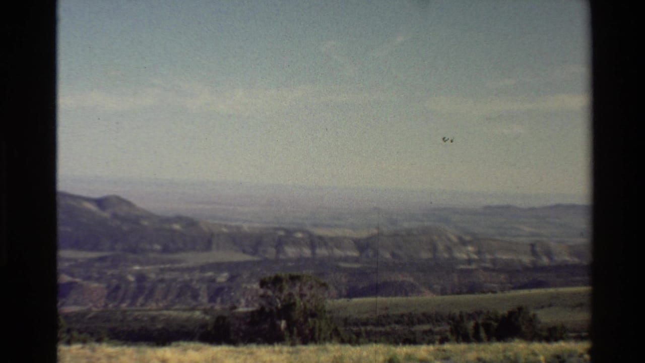 1980 Western USA home-movie frame showing distant ridges, rolling hills, foreground scrub, and dark 8mm frame borders.