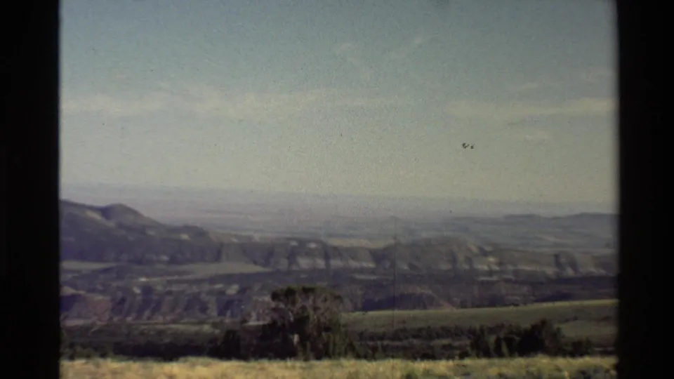 1980 Western USA home-movie frame showing distant ridges, rolling hills, foreground scrub, and dark 8mm frame borders.