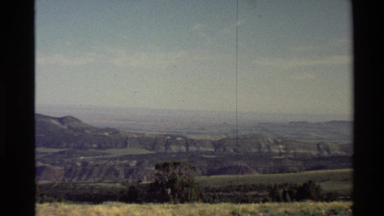 Broad valley and ridged hills under a hazy sky with dark film borders at the sides.
