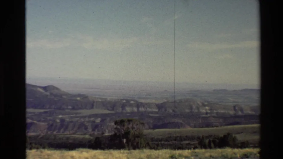 1980 Western USA landscape frame with ridged hills, distant valley floor, light haze, and visible 8mm film border.