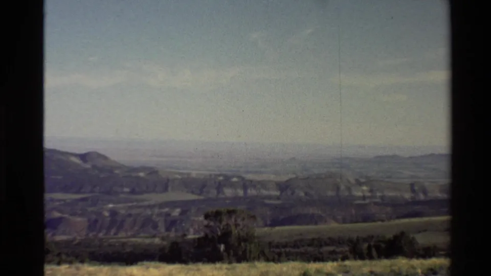 1980 Western USA home-movie still showing rolling terrain, scrub vegetation, distant ridges, and faded 8mm color.