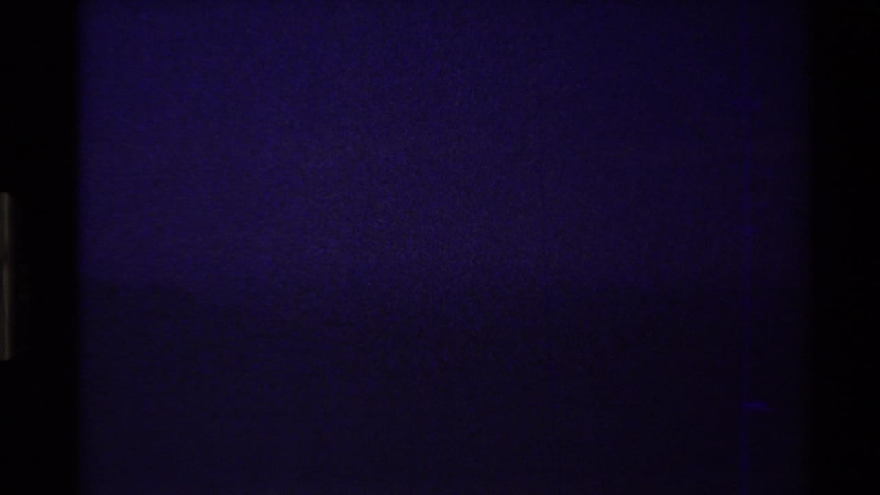 Opening 8mm frame from the supplied 1980 Western USA clip, nearly dark with faint blue-purple grain and visible film-edge artifacts.