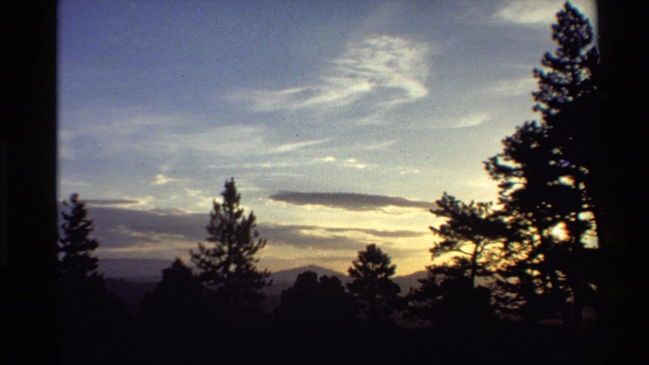 1980 Western U.S. 8mm frame showing dark pine silhouettes, layered clouds, and warm sunset light over distant mountains.