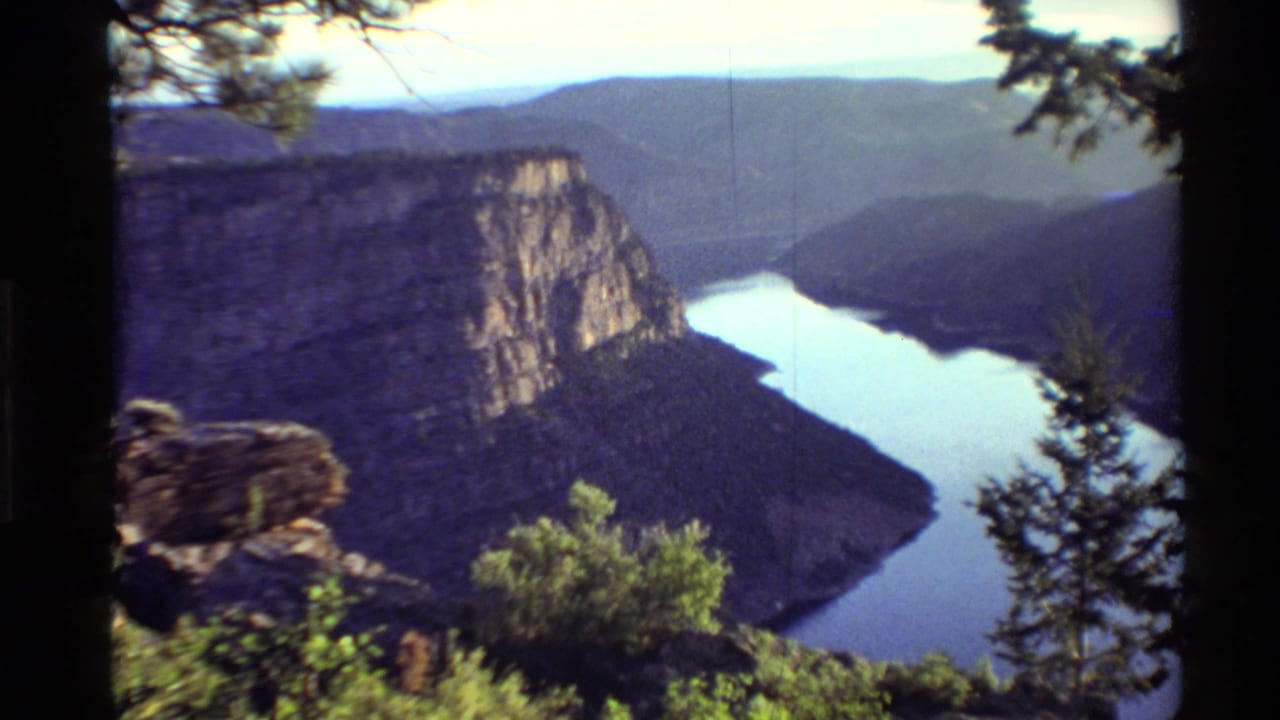 1980 Western USA 8mm landscape showing a river winding between canyon walls, viewed through pines from a high overlook.