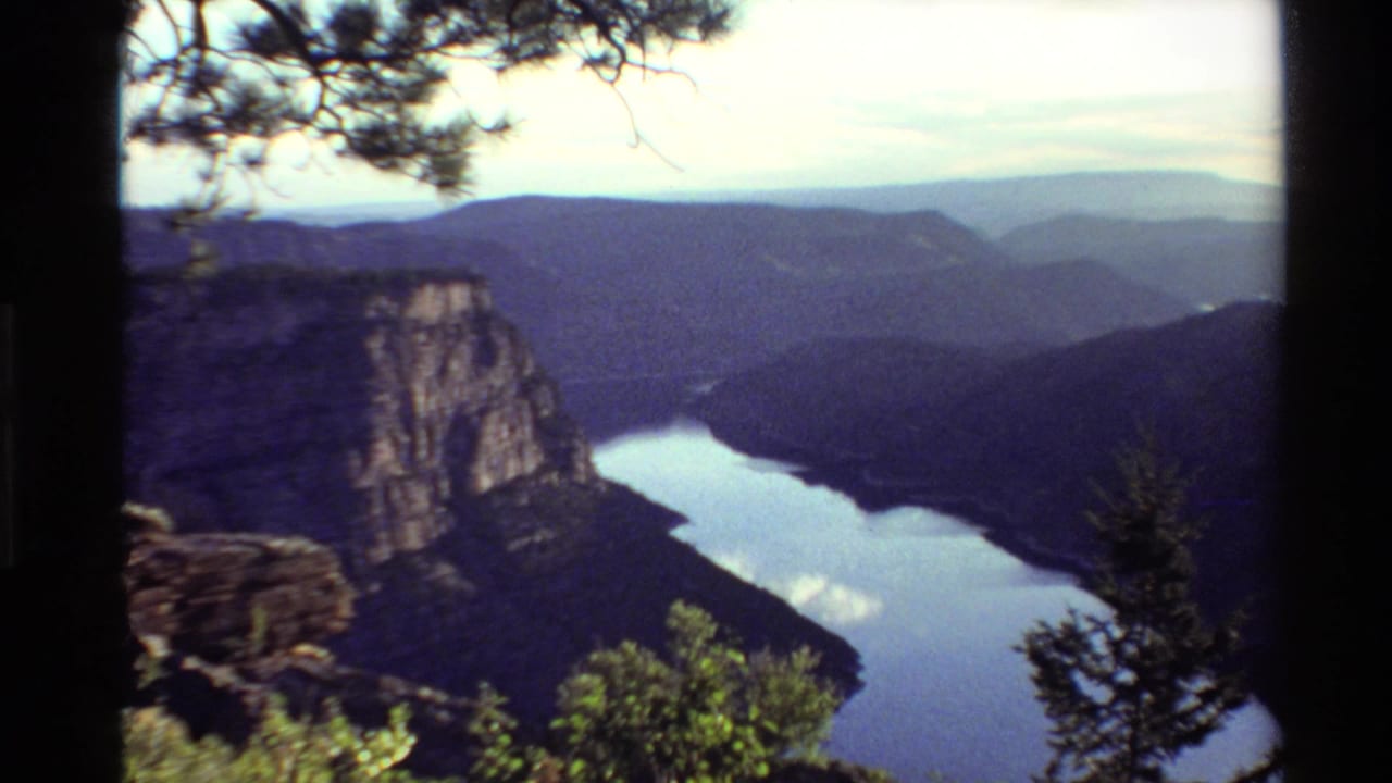 1980 Western United States 8mm view of a winding canyon lake beneath rocky cliffs and forested slopes.