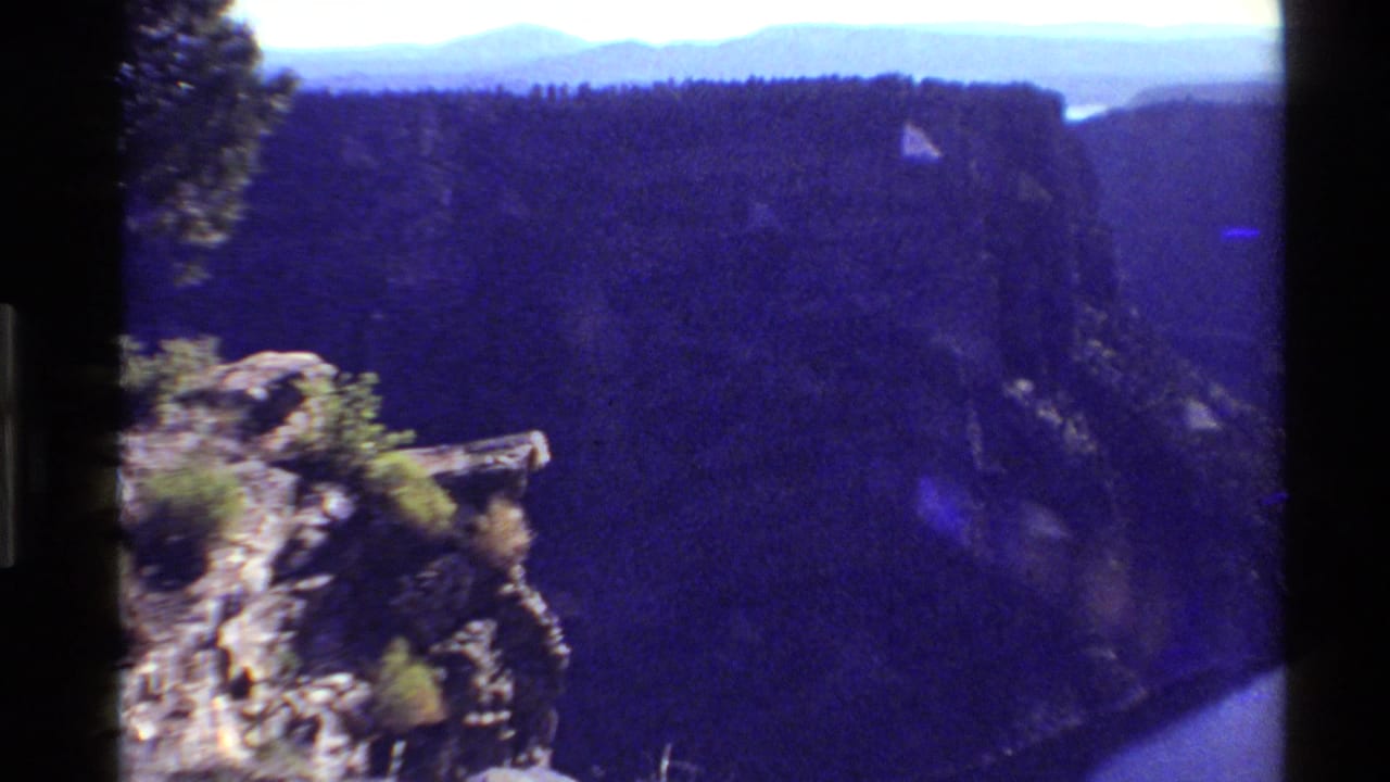 Reported 1980 Western USA 8mm frame showing a rocky overlook, deep canyon shadow, forested ridge line, and pale distant mountains.