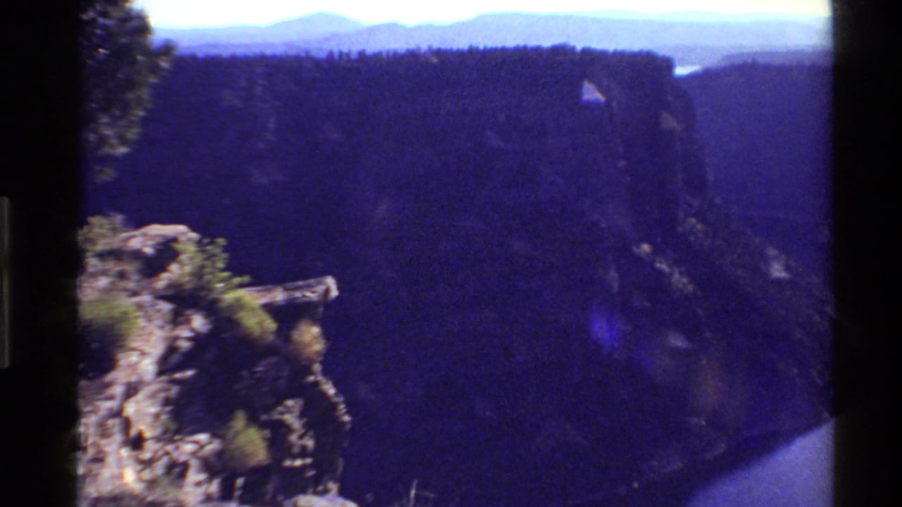 Canyon landscape with rocky foreground, dark ridges, distant mountains, and a river below.