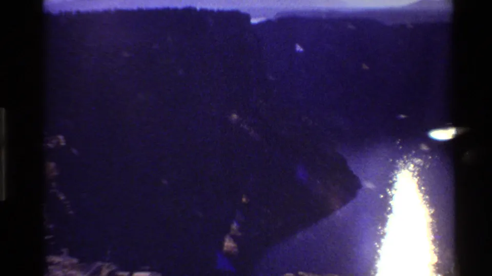 1980 Western U.S. 8mm frame showing a river reflecting sunset light between dark mountain or canyon walls.