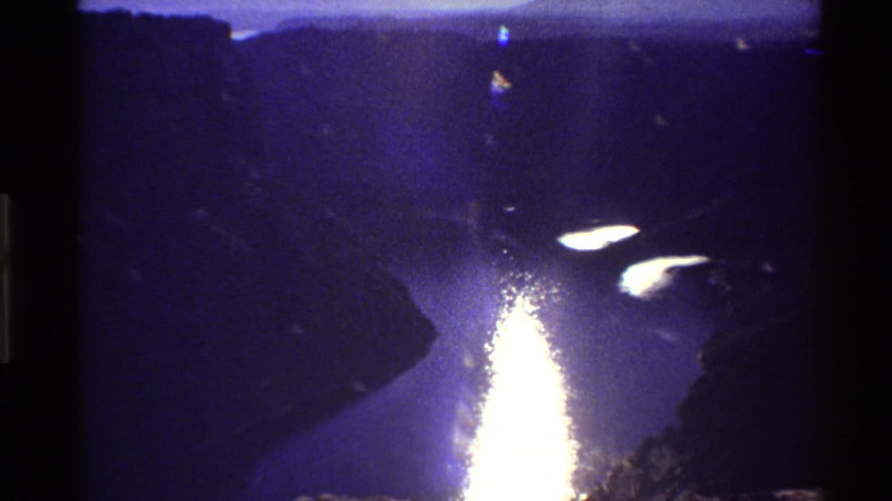Western U.S. 8mm home-movie frame of dusk light reflecting on a river below dark valley walls.