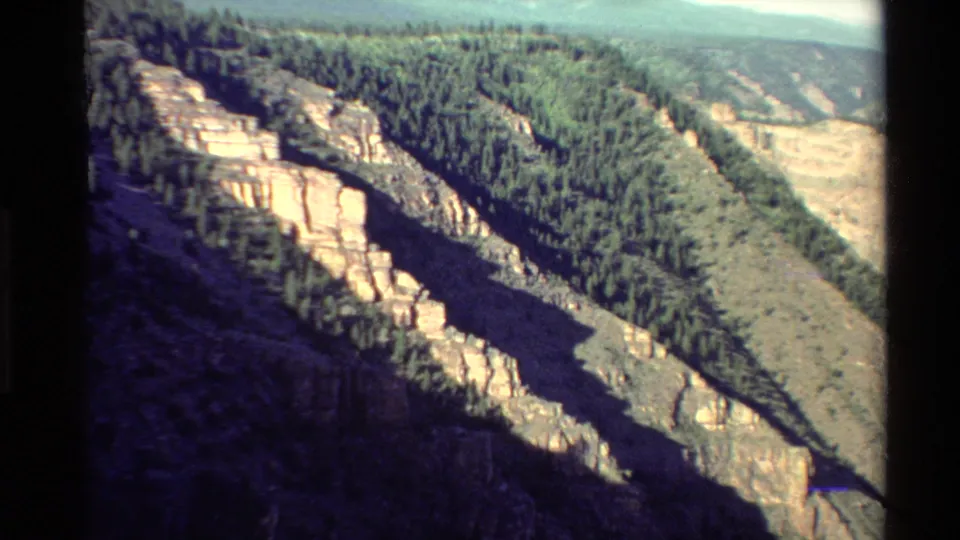 1980 home-movie frame of a Western USA canyon ridge, with pale cliffs, forest, and hazy distant slopes.