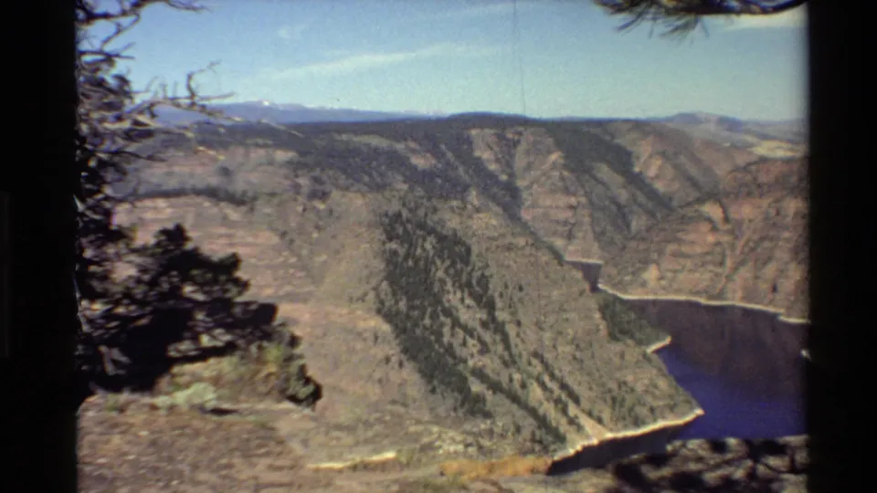 Western USA 8mm view from a canyon overlook, with dark river water below and pine-dotted slopes beyond.