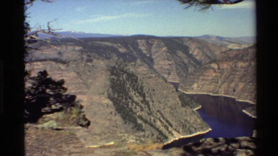 Archival 8mm frame of a Western USA canyon landscape with a river bend, pine ridges, and rocky overlook foreground.