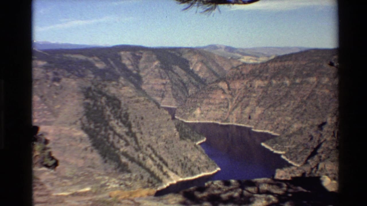 1980 8mm home-movie view of a deep rocky canyon in the Western USA with dark blue water at the base and distant ridges.