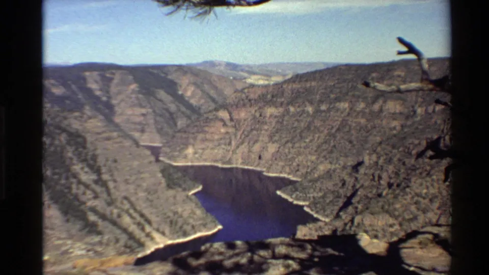 8mm home-movie frame of a rocky canyon overlook in the Western USA, with blue water below and branches at the upper edge.