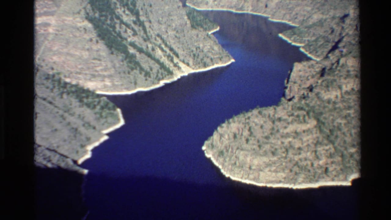 Aerial canyon view with dark water curving past rocky slopes.