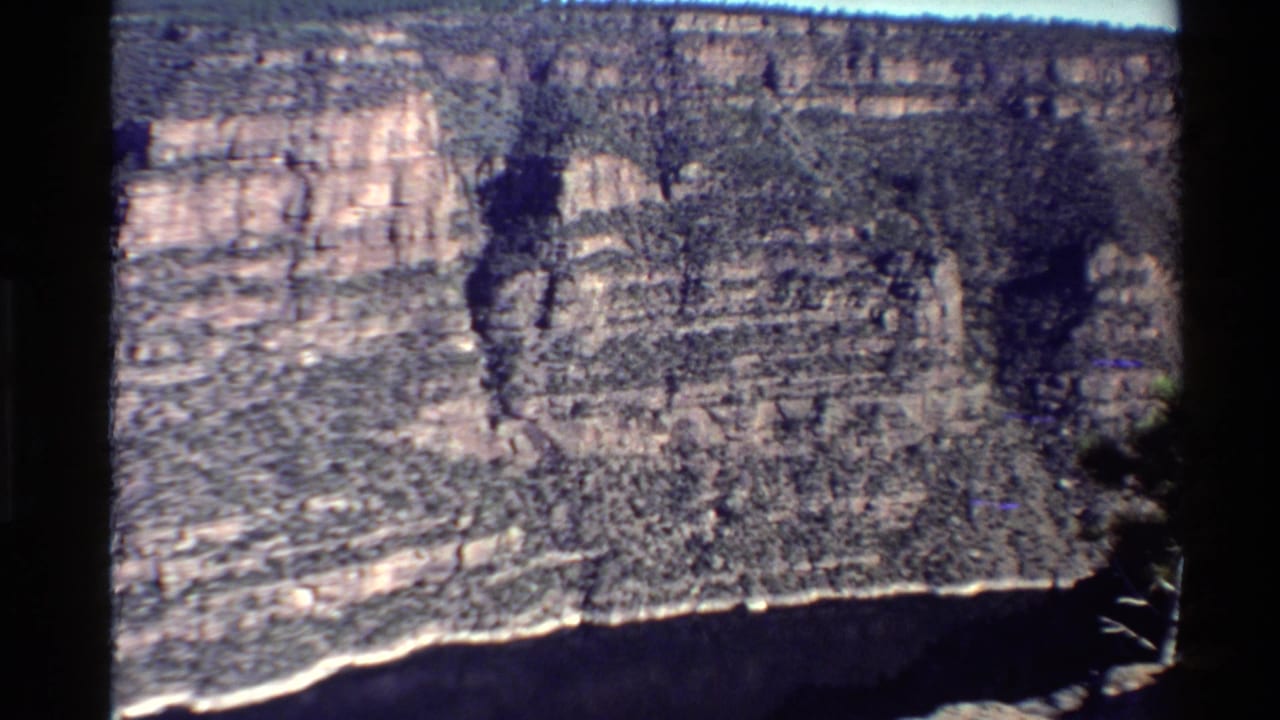 Wide 8mm view of a Western U.S. canyon wall with a dark river bend or shadowed ravine along the lower right.