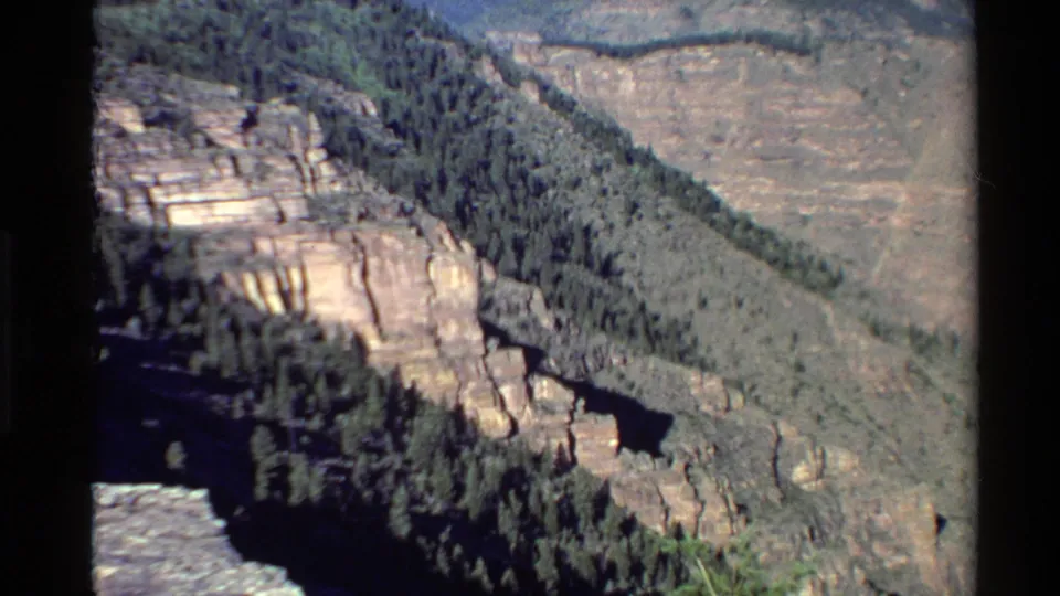 1980 Western U.S. home-movie frame of a canyon panorama with sandstone-like cliffs, dense trees, and ridges in the distance.
