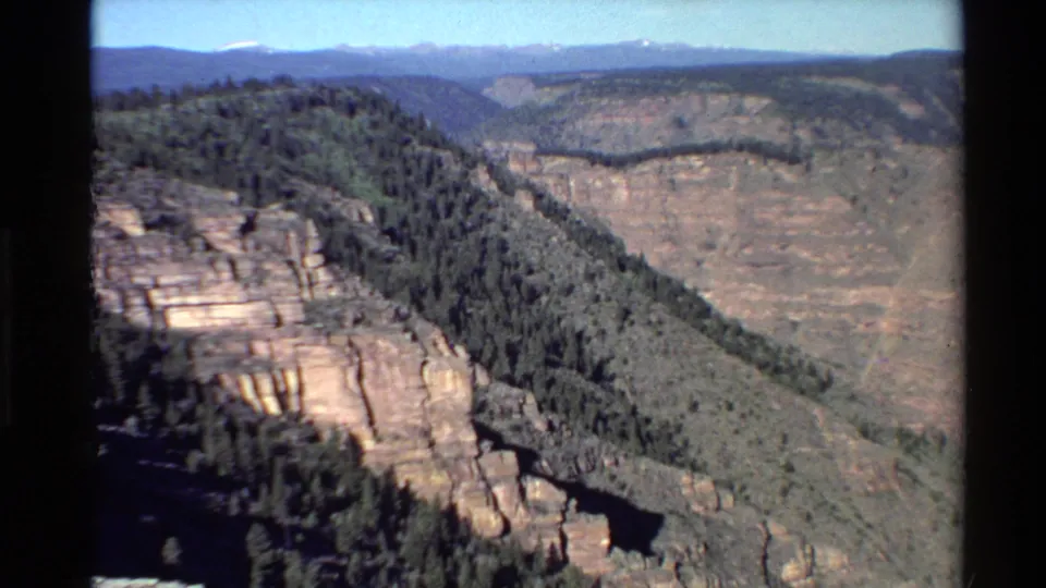 1980 Western U.S. home-movie frame of sunlit rock formations, tree-covered slopes, and a broad canyon wall.