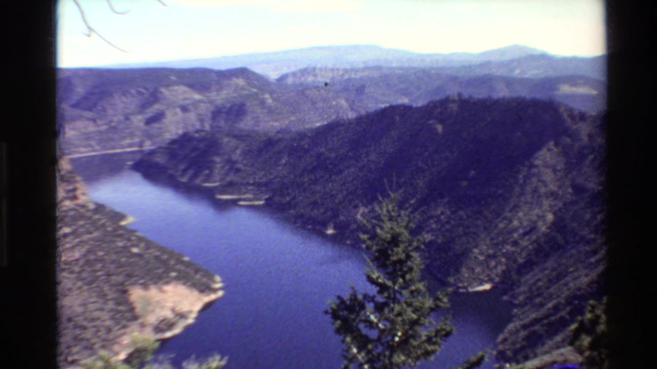 1980 Western U.S. 8mm view of a deep blue lake winding between forested canyon walls and distant mountains.
