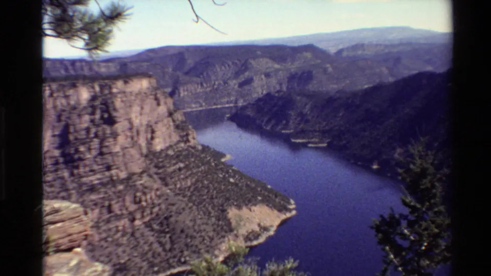 1980 Western USA 8mm view across a reservoir or river below rugged cliffs, with pine branches at the frame edges.