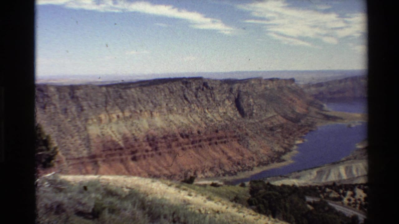 Layered canyon walls above a blue reservoir, framed by dark 8mm borders.