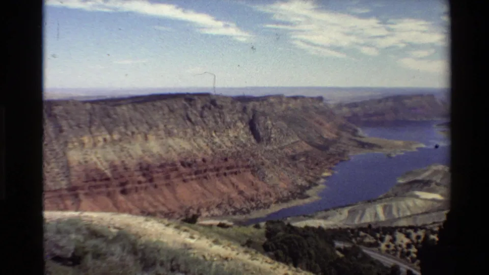 Western U.S. 8mm frame showing a broad canyon basin, blue reservoir, distant mesas, and soft film grain.