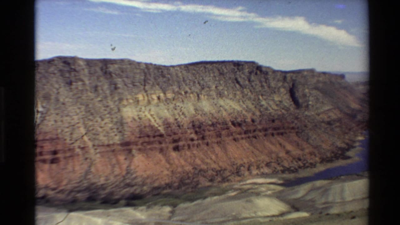 Aerial 8mm view of a Western U.S. canyon with layered cliffs and a blue river bend visible along the lower right.