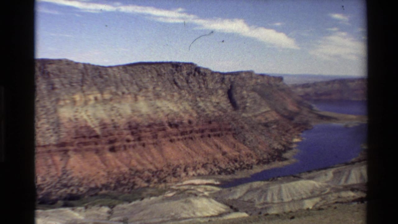 Western U.S. canyon landscape in 1980 8mm footage, showing a winding blue river beside red-brown cliffs and distant terrain.