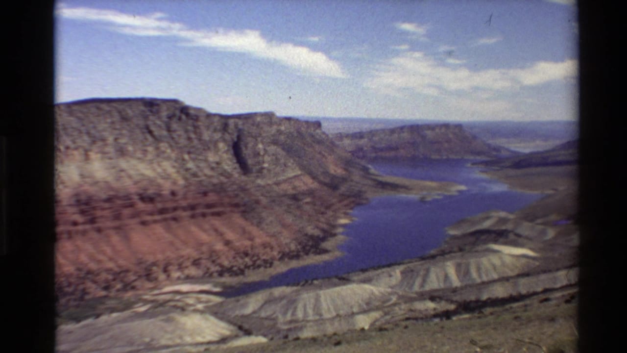 1980 Western U.S. 8mm frame showing a blue reservoir winding below red and tan canyon walls from a high overlook.