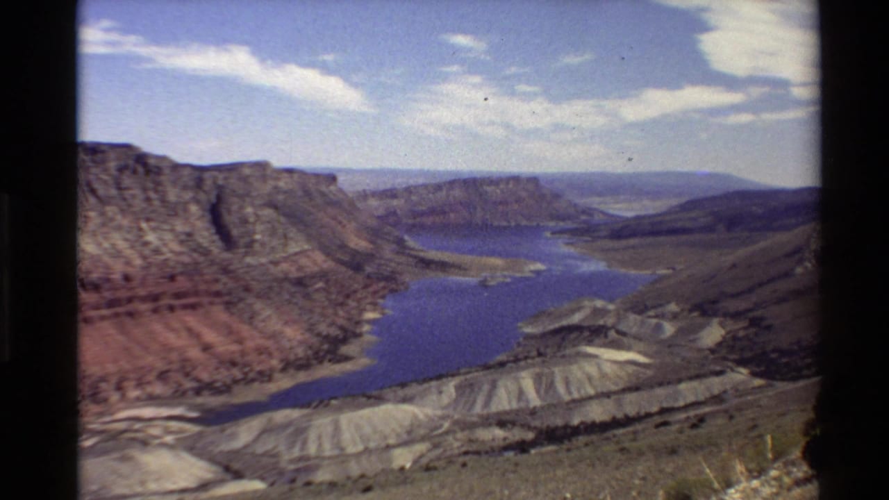 Final 8mm frame holds on the reservoir overlook, with layered red and tan hills, distant ridges, and scattered clouds.