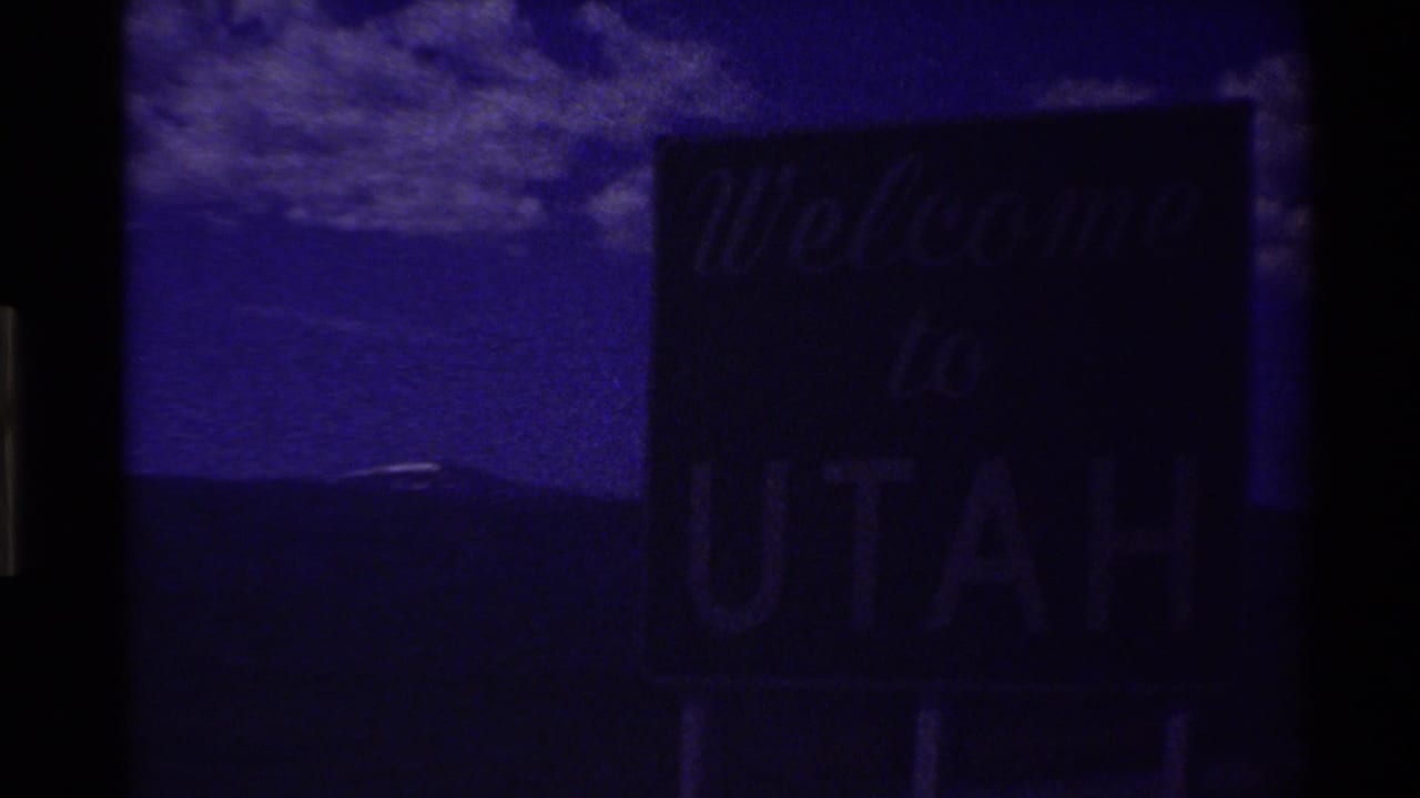 Dark opening frame of 1980 8mm footage showing a barely visible Welcome to Utah sign with heavy purple cast and gate borders.