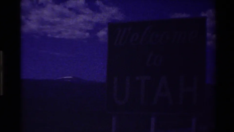 Dark opening frame of 1980 8mm footage showing a barely visible Welcome to Utah sign with heavy purple cast and gate borders.