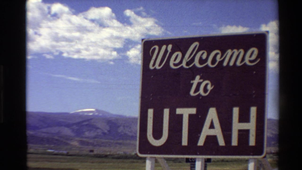 Final 1980 8mm frame with the Welcome to Utah sign at right, open Western landscape, distant mountains, and bright clouded sky.